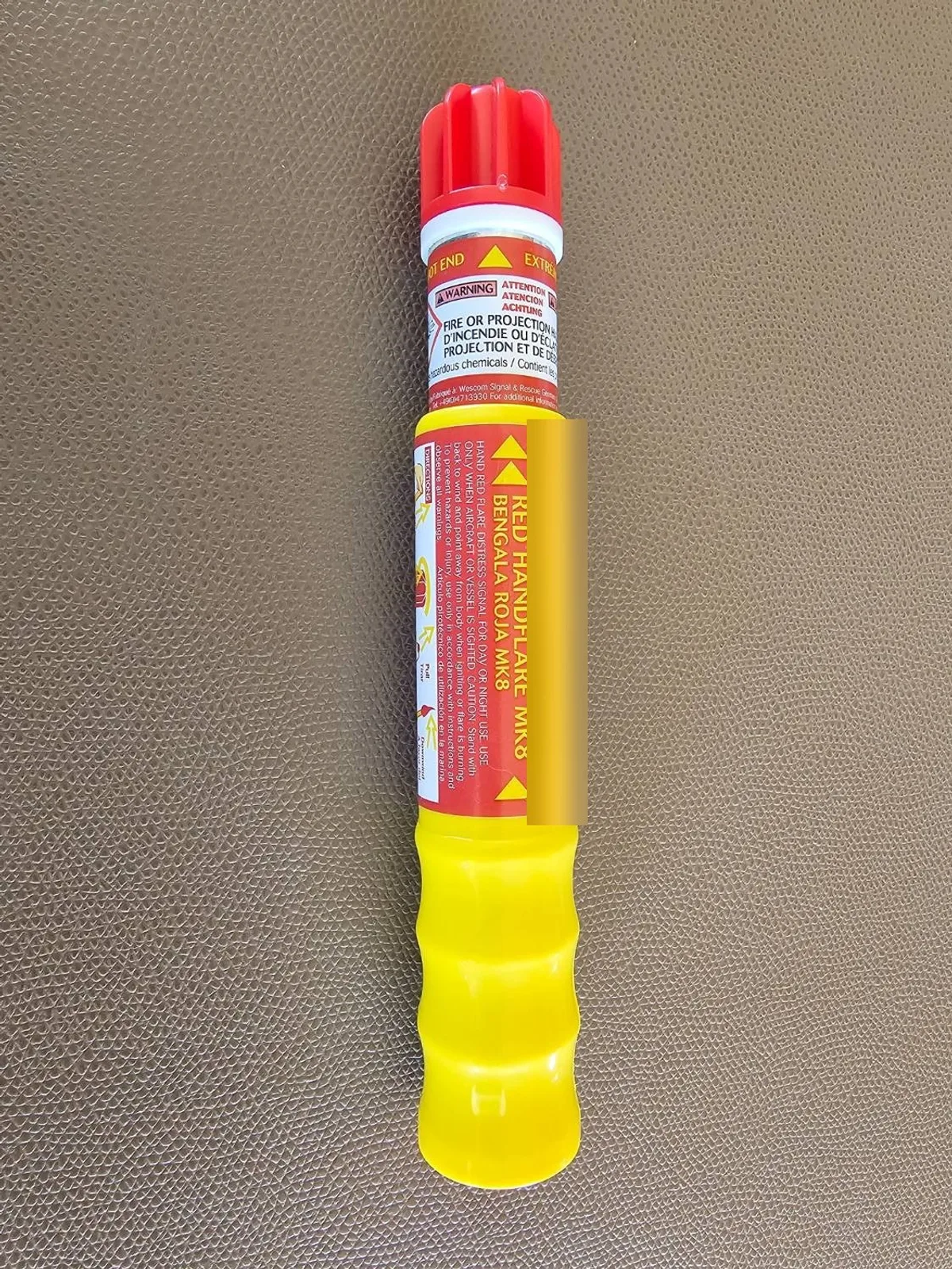A red handheld flare lying on a plain surface, with the maker's label and printed steps on the casing. The date strip is blurred.