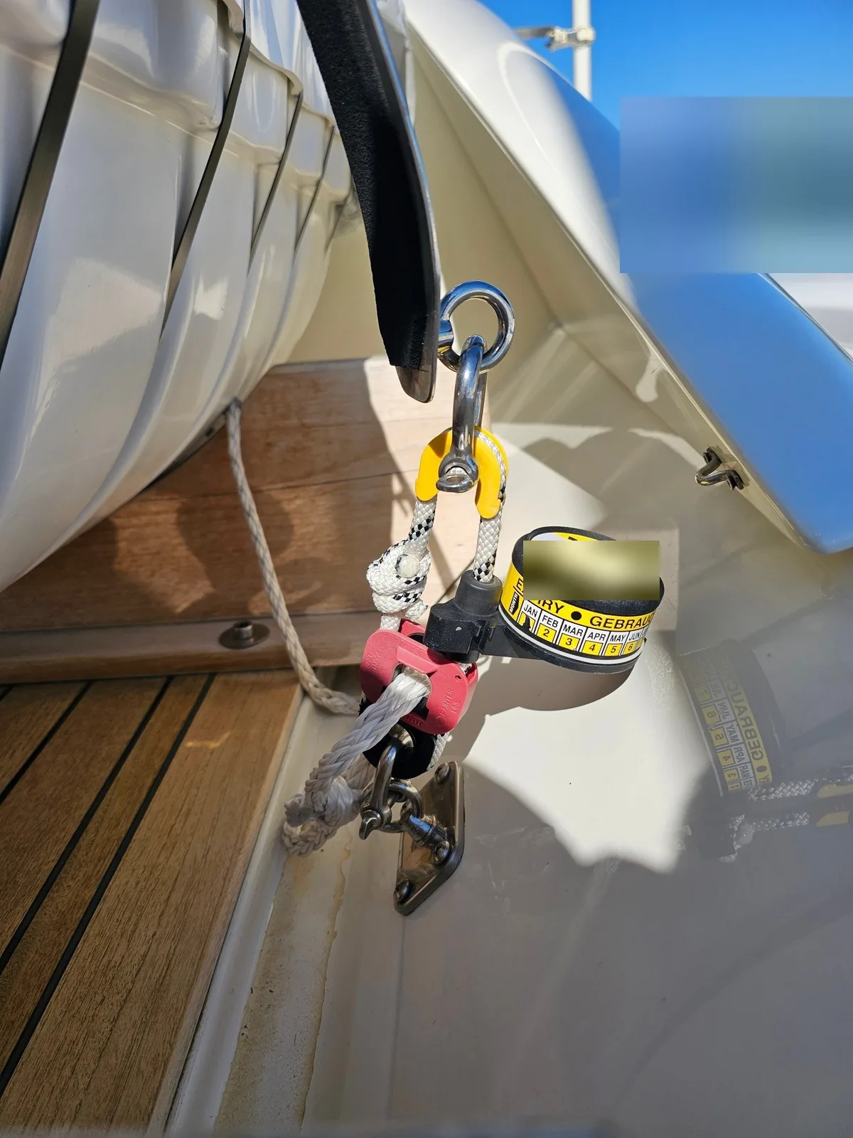A hydrostatic release unit hanging beside a liferaft cradle, with its lashing. The label on top of the unit is blurred.