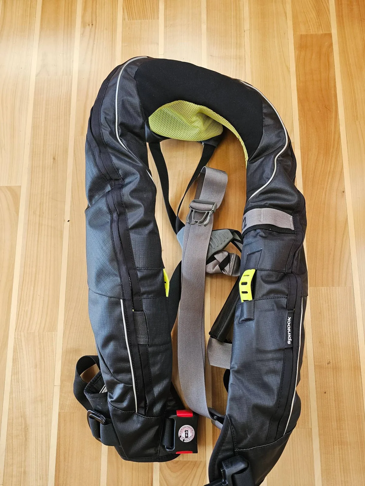 A lifejacket laid flat on a wooden deck, with its harness strap and buckle.
