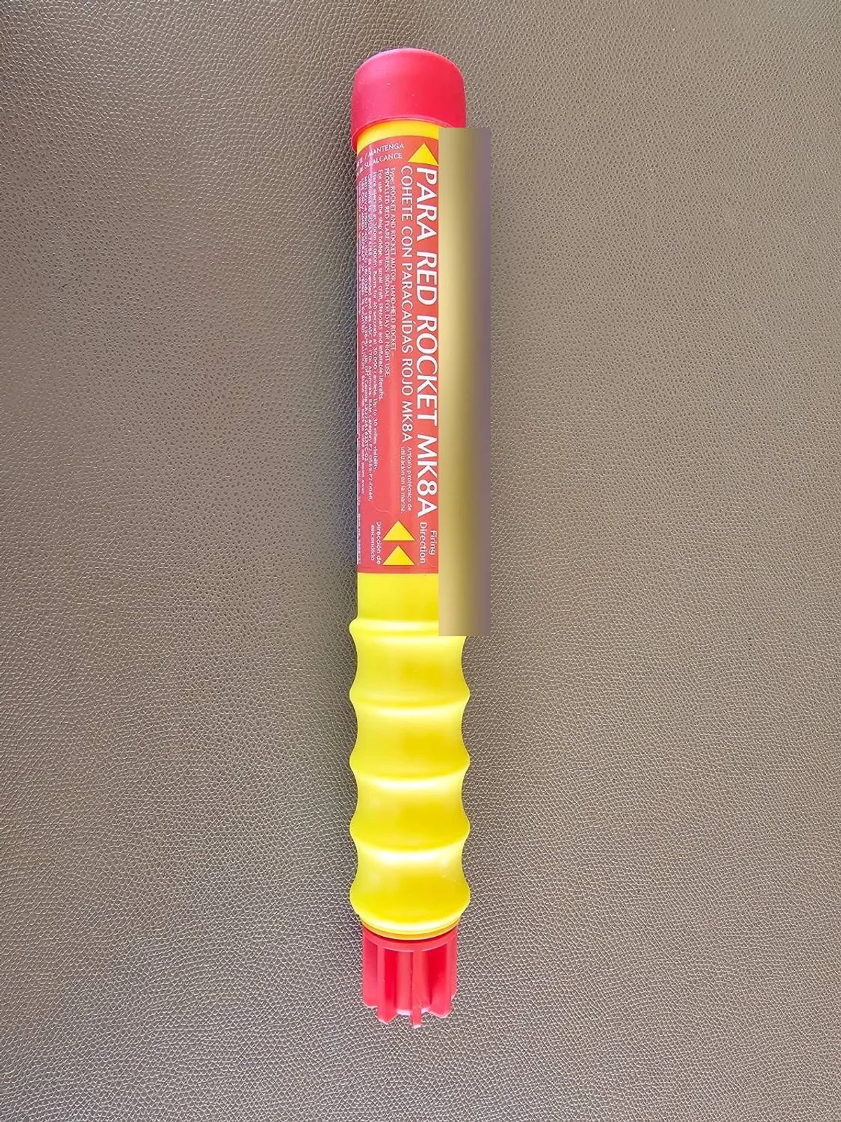 A red parachute rocket flare lying on a plain surface, with the maker's label and printed steps on the casing. The date strip is blurred.