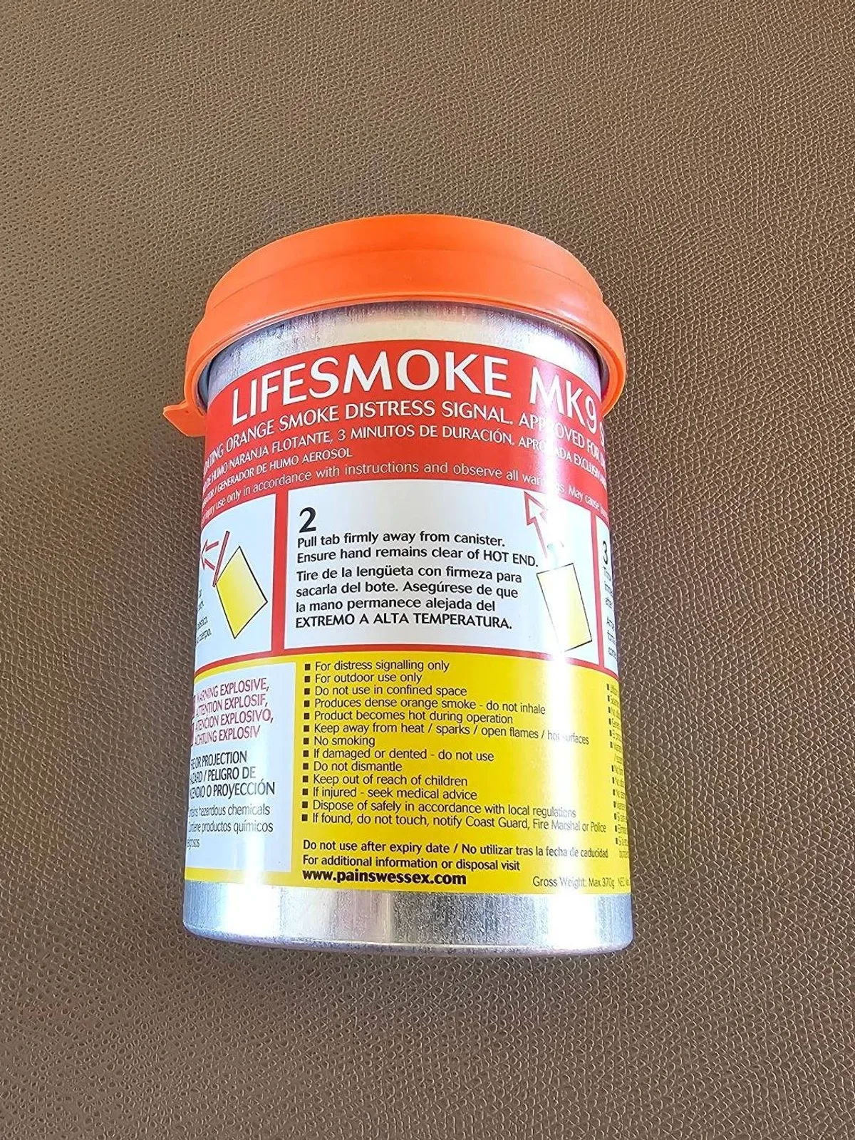 An orange smoke canister standing on a plain surface, with the maker's label and printed steps on the casing.