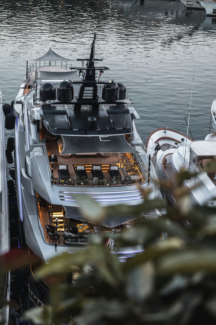 A superyacht stern-to in harbour at dusk, deck lights on